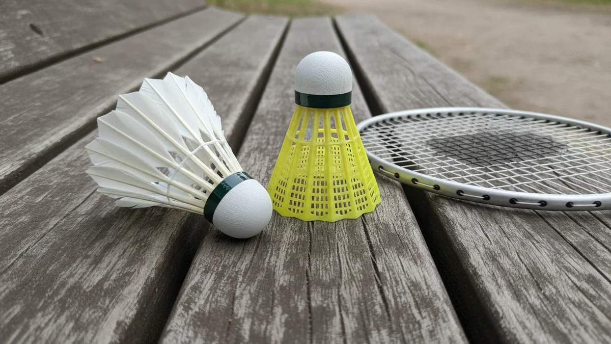 Péřový a plastový badmintonový míček vedle rakety