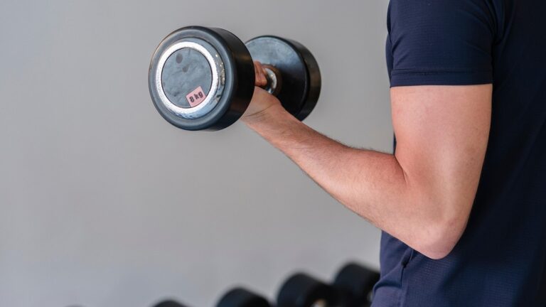 Muž v posilovně cvičí s jednoruční činkou bicepsový zdvih
