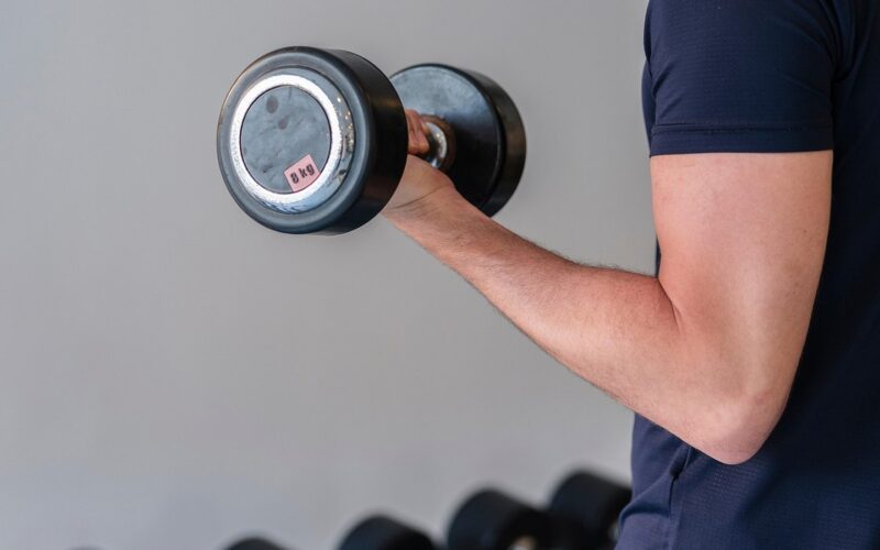 Muž v posilovně cvičí s jednoruční činkou bicepsový zdvih